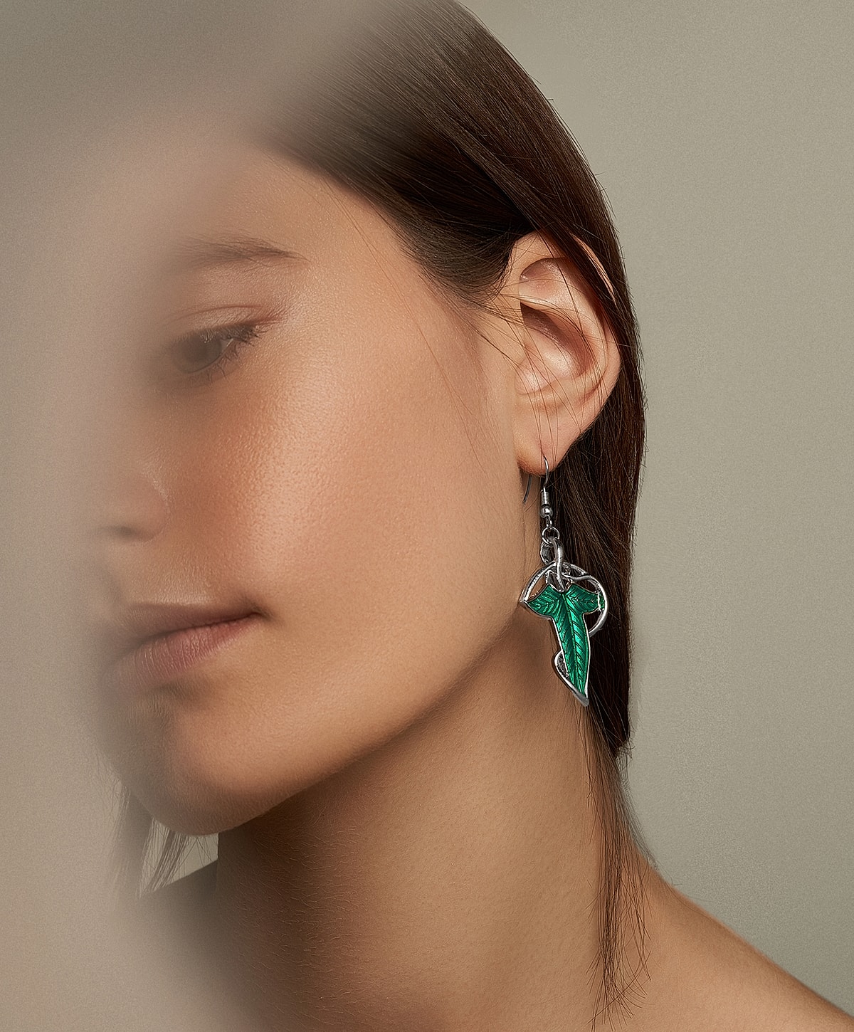 Model wearing green leaf earrings, neutral background.