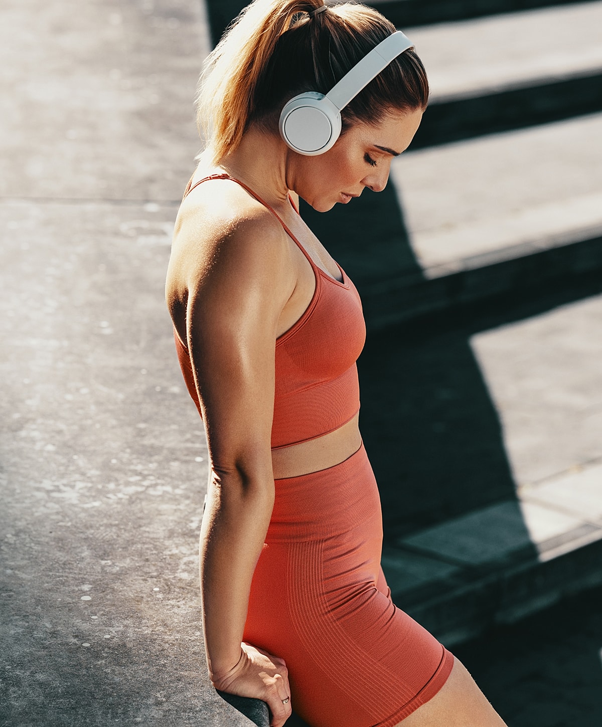 Woman in workout attire wearing headphones outdoors.