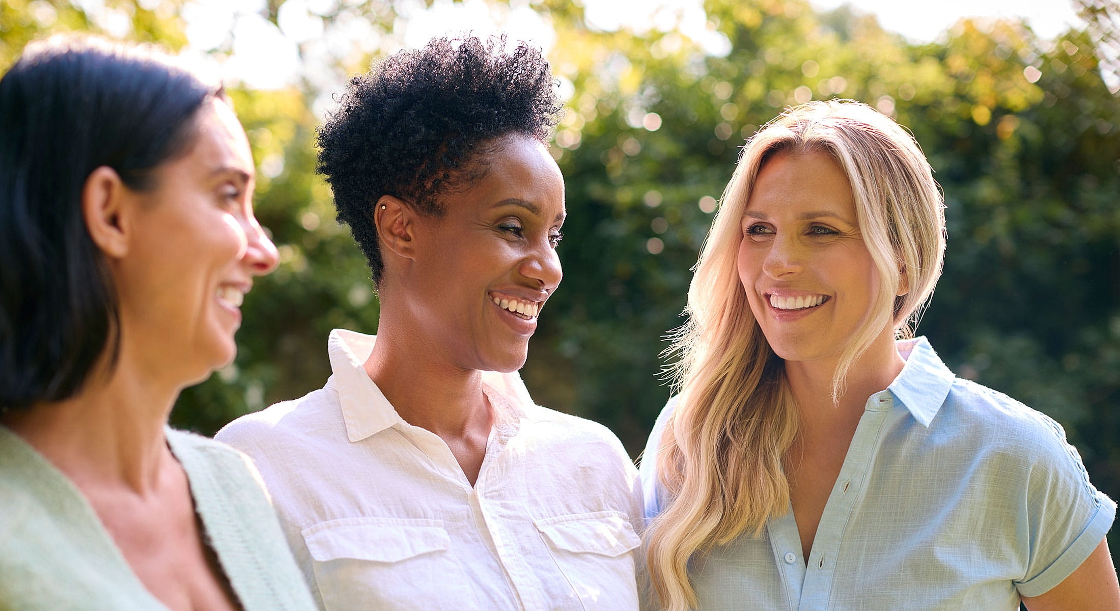Three women smiling in a natural setting.
