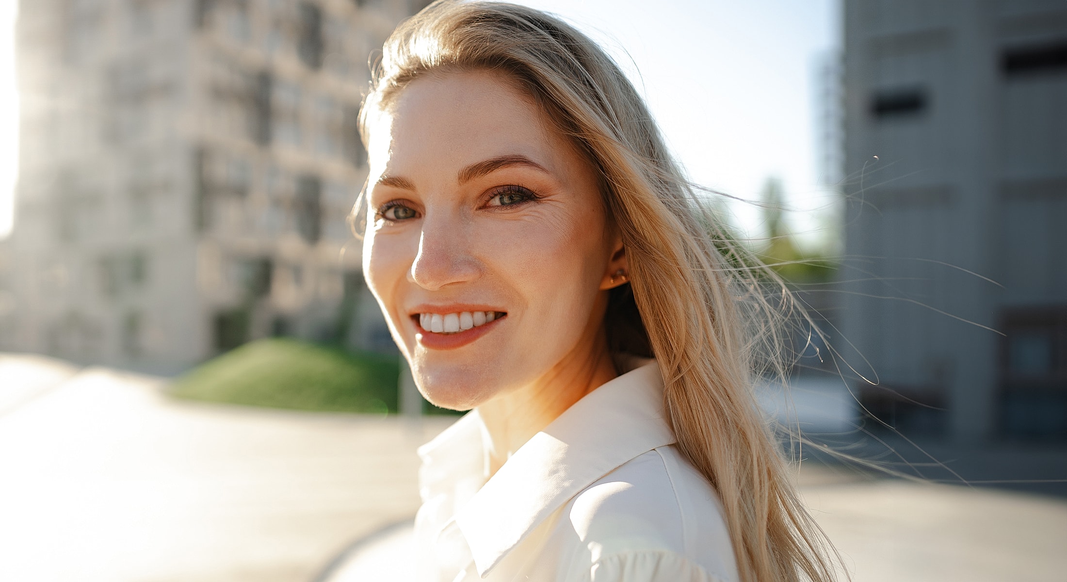 Smiling woman with long hair outdoors in sunlight.