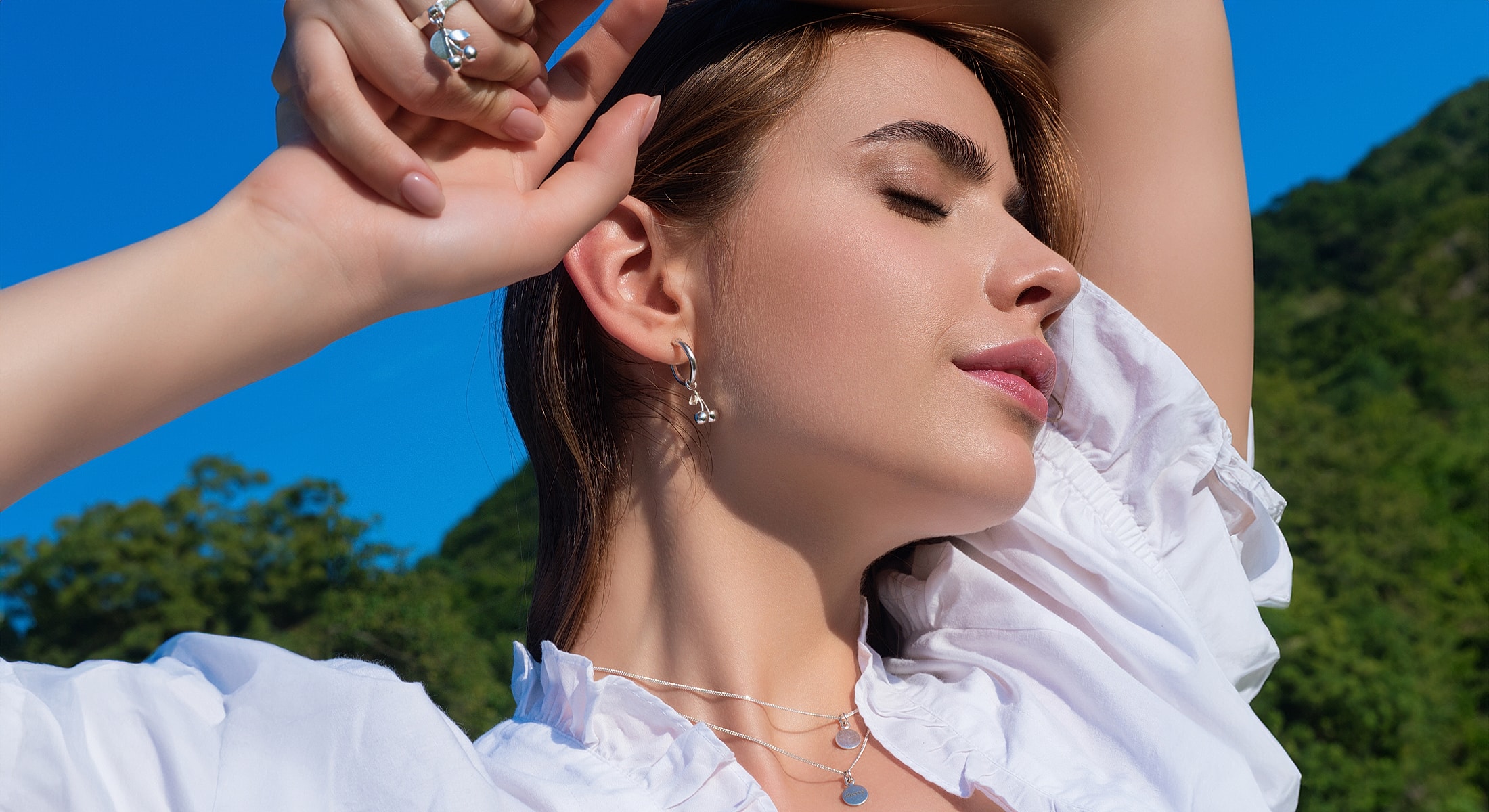Model wearing jewelry against a blue sky.